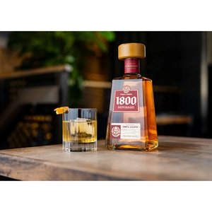 1800 Tequila Reposado bottle with a glass on a table.