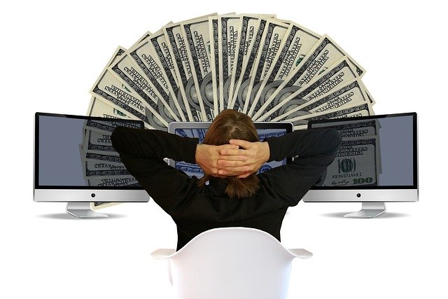 Person in front of computer monitors with a fan of dollar bills, symbolizing Make1M financial success.