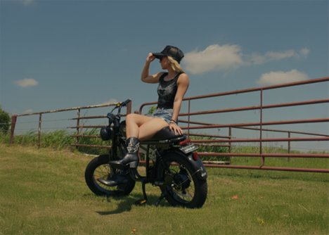 Rider sitting on a moped ebike in an open field on a sunny day.