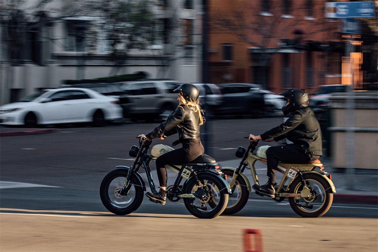 Two riders on moped ebikes cruising through city streets.