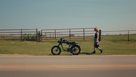 erson walking beside a moped ebike on a rural road.